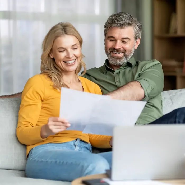 Ein Mann und eine Frau sitzen auf einer Couch und schauen auf ein Blatt Papier.